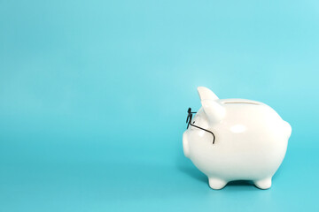 White ceramic piggy bank wearing reading glasses on blue teal background, from side view. Concept for money savings plan for retirement, aged society, or financial accounting