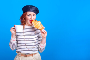 woman with cup and croissant in studio on a blue background