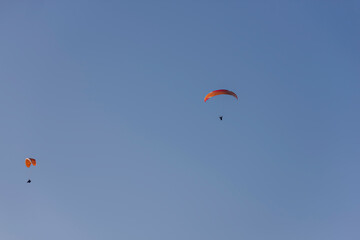 Paragliders with multi-colored parachutes fly high in the clear blue sky over steep cliffs. Parachuting, adrenalitis, love of height, risk, freedom of action. Desire to be able to fly