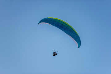 Paragliders with multi-colored parachutes fly high in the clear blue sky over steep cliffs. Parachuting, adrenalitis, love of height, risk, freedom of action. Desire to be able to fly