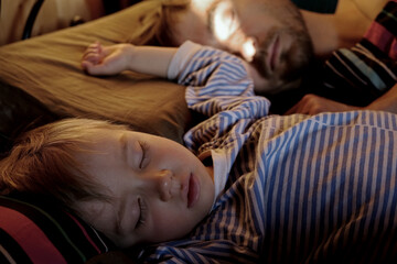 Obraz na płótnie Canvas Cute toddler son and his father sleeping together on bed in bedroom at home. Real lifestyle family photo taken early morning. Fathers day concept.