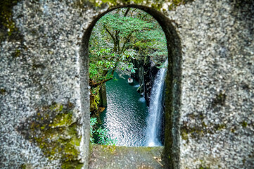 A nature landscape view through stone wall arch of fresh rain forest waterfall of Takachino George, Miyazaki, Kyushu, Japan
