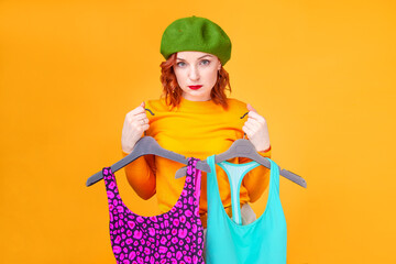 woman in a green beret holds hangers with clothes on a beige background in the studio