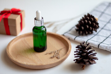 Green dropper bottle serum on wood plate. Natural facial essential oil or serum packaging on white fabric background. Beauty product branding mock-up.  Cosmetic skincare concept. Cruelty-free.  