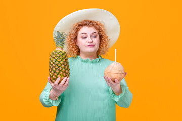 blond woman with pineapple and coconut in hands on a yellow background in the studio