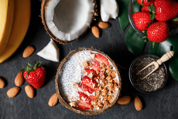  Smoothie bowl in coconut shell with strawberries, chia seed pudding, granola