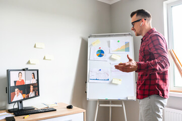 Confident young man conducts webinar, business training online. Online coach stands near flip chart...