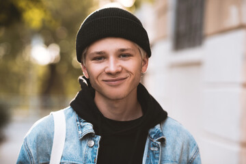 Smiling teen boy 16-18 year old wearing black knitted hat, hoodie and denim jacket outdoors at sun...