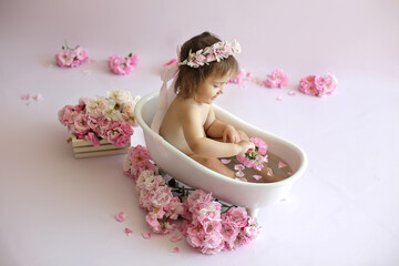 A little girl is bathing in a bath with rose petals. Photo session on your birthday. Stylized shooting.