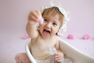 A baby in a cap takes a bath and shows her tongue. Happy girl happily bathes.
