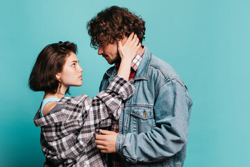 Young couple isolated over blue background. Stand close to one another. Hipster man and woman touch each other and look into eyes. Love, tenderness.