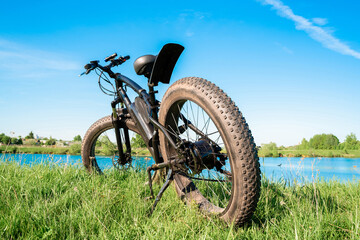 Fototapeta na wymiar Black electric bike with thick wheels on the grass near the lake. Fatbike