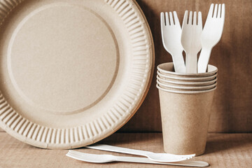 Wooden forks and paper cups with plates on kraft paper background. Eco friendly disposable tableware. Also used in fast food, restaurants, takeaways, picnics. Copy, empty space for text