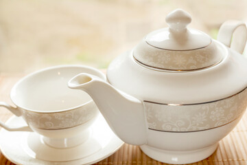 A cup on a saucer and a teapot on a table in the morning