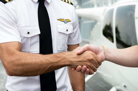Teamwork of young caucasian handsome man in pilot uniform shaking hands together for say hello ready to flight and helicopter platform background.Two pilot man shaking hands to achieve success.