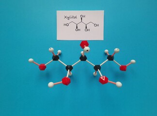 Molecular structure model and structural chemical formula of xylitol molecule. Xylitol is a polyalcohol (sugar alcohol), used as a food additive and sugar substitute in toothpaste and chewing gum.