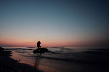 Fototapeta na wymiar silhouette of a man standing on the beach at sunrise