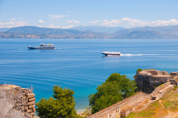 View from ancient fortress ruins to a sea with ship and other shore with mountains at the horizon