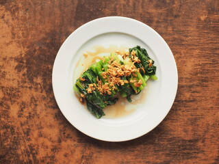 Top view stir fried Chinese kale with oyster sauce with crispy golden fried garlic on wooden table