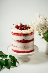 Red berry cake decorated with cherry berries and white cream, among lilac flowers and green leaves. Food photography. Advertising and commercial design.