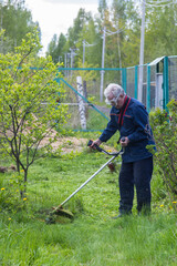 a worker mows grass and weeds with a lawn mower in the country