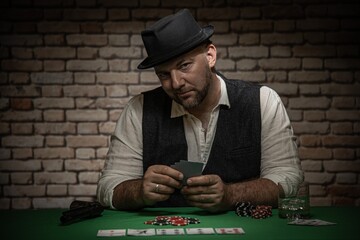 Poker player with cards and playing chips a the poker table -  poker in a dark back room with a brick wall