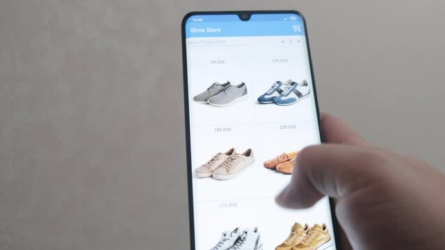 A young man is shopping through a mobile app. Buys shoes online. Online shopping. Close up. Mobile application online store.