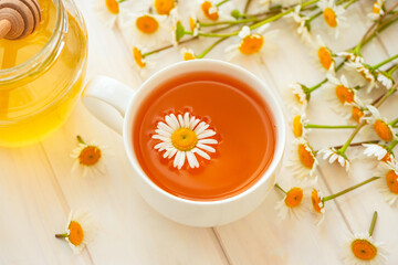 Herbal tea with fresh chamomile flowers and honey on white wooden background. Soft focus