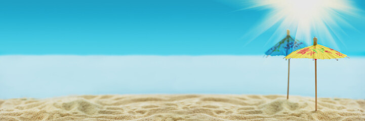 Fototapeta na wymiar Banner 3:1. Sun umbrellas on sandy beach with blurry blue ocean and sky. Social distancing or COVID-19 protection at summer holidays. Summer background. Soft focus