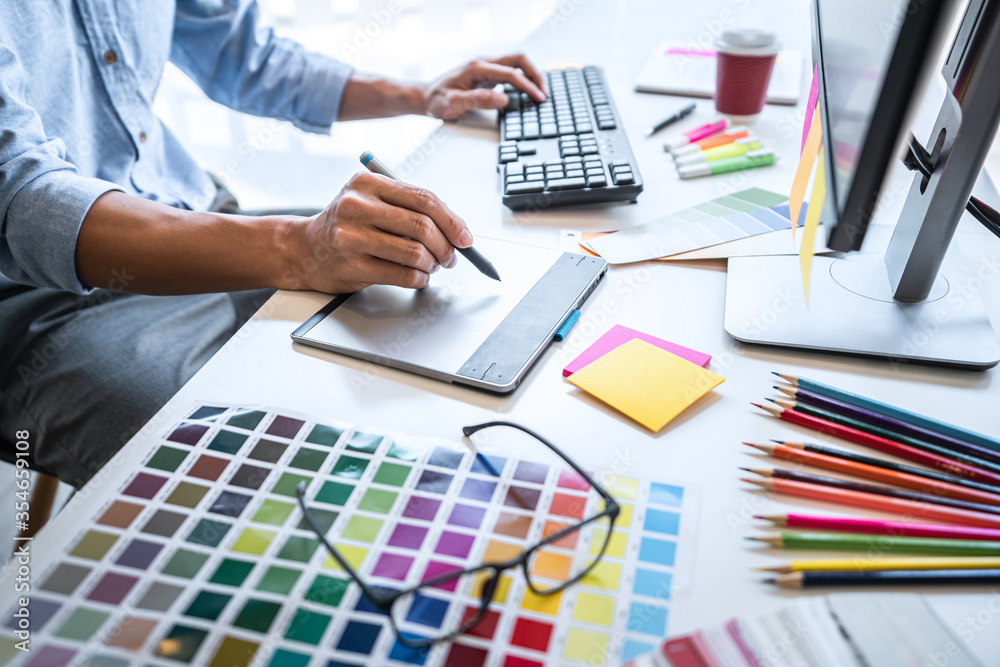 Poster Image of male creative graphic designer working on color selection and drawing on graphics tablet at workplace with work tools and accessories in workspace
