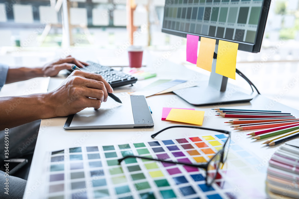 Poster Image of male creative graphic designer working on color selection and drawing on graphics tablet at workplace with work tools and accessories in workspace
