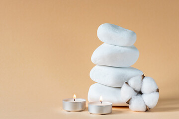 White zen stones with candles and cotton flower on beige background. Spa salon banner concept. Massage stones, relax and alternative medicine concept.