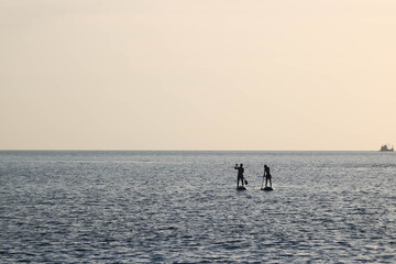 Couple of man and woman paddle on the surf board happily together under the sunset sky
