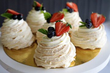   Pavlova cakes decorated with white cream and fresh berries lie on a white plate on a gold stand