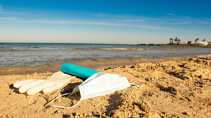 Protective mask and glove, sun lotion on the beach. Coronavirus concept.