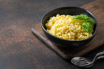 Homemade hot pasta ptitim decorated basil leaves on brown background. Close up. Space for text.