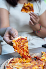 Female’s hand holding slice a pizza out of the wooden tray..