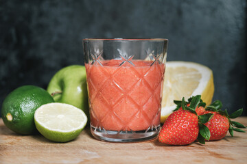 A glass of red cocktail with fruit on the wooden table and dark background. Apple, lime, lemon, strawberry.