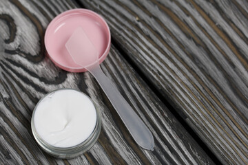 Plastic bottle with cream. The cover is removed and lies nearby. Shovel for cream. Plastic bottle with cream. The cover is removed and lies nearby. Shovel for cream. The background of pine boards.