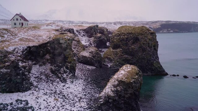 A house is seen overlooking Arnarstapi Harbor on the Sn&aelig;fellsnes Peninsula of Iceland with snow on the ground.