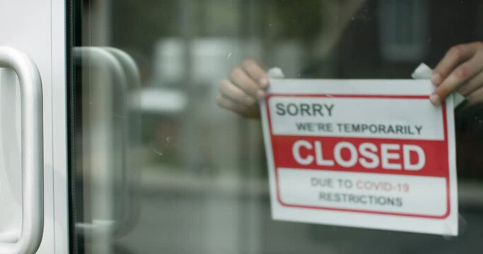Closed for business due to covid. Small shop puts closed sign up on storefront. Business closes due to covid. A sign put up on shopfront. Shot in slow-motion in 4k.