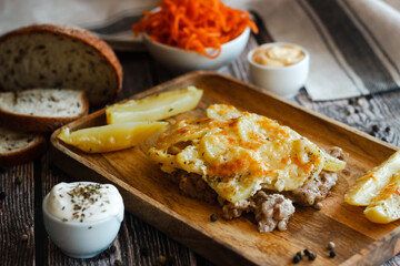 Tasty casserole with meat, potatoes, cheese and spices. Casserole served with carrot, bread and sour cream. Russian traditional dish. Dish on a wooden table