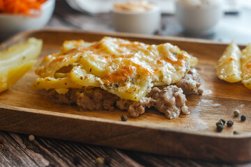 Tasty casserole with meat, potatoes, cheese and spices. Casserole served with carrot, bread and sour cream. Russian traditional dish. Dish on a wooden table