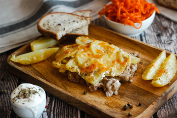 Tasty casserole with meat, potatoes, cheese and spices. Casserole served with carrot, bread and sour cream. Russian traditional dish. Dish on a wooden table