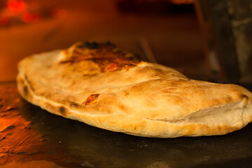 A baker's calzone pizza with a traditional Mediterranean wood-burning oven (wood-fired oven),Italian food-calzone stuffed.Close up