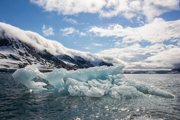 Fototapeta premium An Iceberg in the sea in front of Mountains in Svalbard