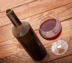 Glass and bottle of red wine unusually on wooden background.