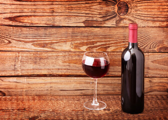 Glass and bottle of red wine unusually on wooden background.