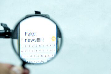 Isolated Hands holding a phone and magnifier with 'fake news" wording in the white background
