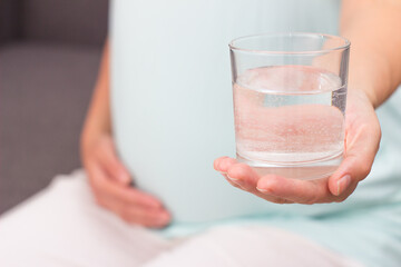 Pregnant drinks mineral water. The pregnant woman holds a glass of mineral water.